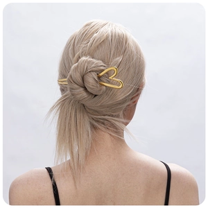 Detail showing a golden heart-shaped metal hairpin styling a bun hairstyle on blonde hair