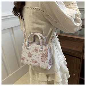 Close-up of small beige handbag featuring purple butterfly prints and gold metal hardware