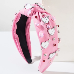 Pink headband with rhinestones and heart arrow charms on a white geometric stand