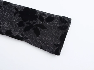 Detail of black knit fabric with glitter finish and floral flocking on the dress sleeve