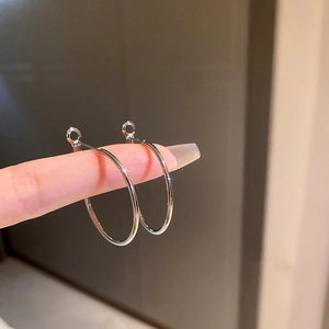 Gros plan de boucles d'oreilles créoles argentées tenues pour montrer la taille