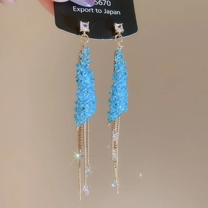 Macro detail of blue crystal earrings with long gold chain tassels and sparkling effect