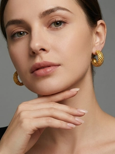 Close-up of geometric C-shaped gold mesh earrings with embossed dot texture on a model