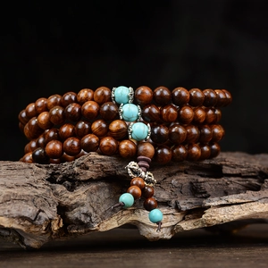 Macro detail of 108 black rosewood prayer beads with turquoise accents on bark