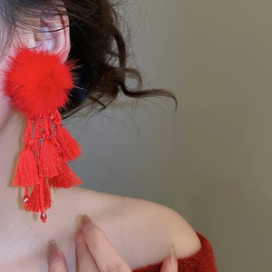 Detail of elegant red pompom fringe earrings worn by a model in a warm setting