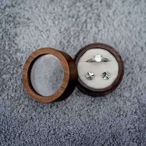 Top view of a round wooden ring box with a silver diamond ring and clover earrings