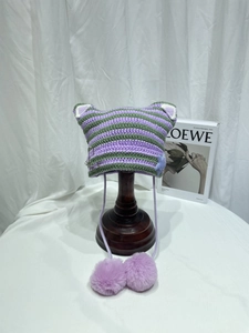Detail of purple and green striped crochet cat ear beanie with large pom-poms