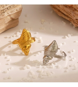 Close-up of gold and silver seashell rings with textured spiral patterns on beach stones