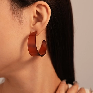 Close-up of model wearing large amber resin C-shape hoop earrings with tortoiseshell pattern