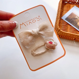 Close-up of handmade lace bow hair clip and embroidered bear hair tie on display card