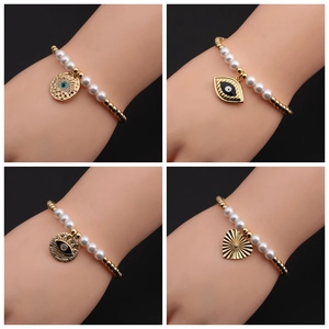 Bracelet perles dorées et perles blanches avec breloques œil et cœur au poignet