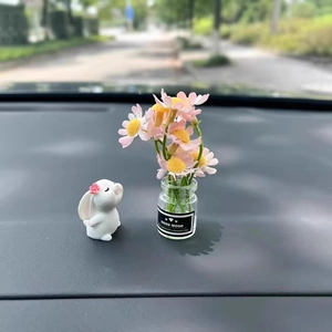Miniature bunny figurine and glass flower vase on car dashboard with jasmine decor