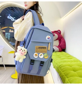 Blue nylon school backpack with decorative badges and a plush bear pendant accessory
