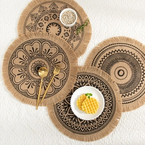 Set of four round jute placemats with black floral patterns and bohemian tassels