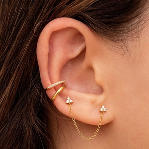 Close-up of golden flower stud earrings and cuff set with diamond accents on model ear
