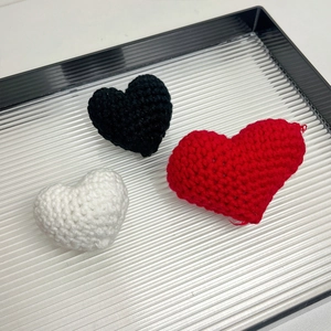 Handmade knitted heart brooches in red, black and white colors on a dark display tray