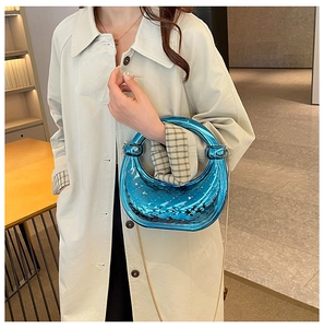 Detail of blue metallic moon bag with quilted texture held by model in beige trench coat