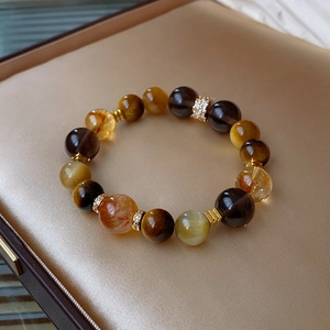 Detail view of white crystal bracelet with natural tiger eye and golden accents on satin