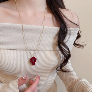 Detail of a vintage red flocked grape tassel necklace worn by a model on a gold chain