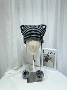 Detail of knit cat ear beanie with striped pattern, metal pin, and plush pom poms
