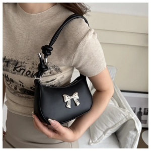 Detail of black matte leather underarm bag featuring a silver metal bow and knotted strap