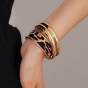 Détail du bracelet en cuir léopard et joncs dorés polis portés sur le poignet