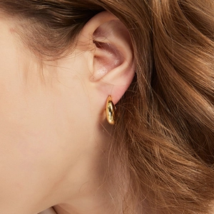 Side view of chunky gold teardrop hoop earrings worn by a model in a minimalist style