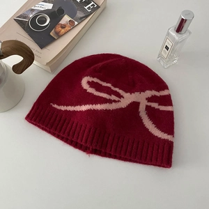 Detail of red knit hat with pink bow pattern on white table in an aesthetic setting