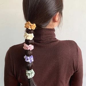 Five assorted floral scrunchies in vibrant colors styled on a ponytail hairstyle