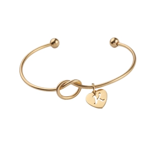 Detail of gold knot open cuff bracelet featuring a heart charm with letter K engraving