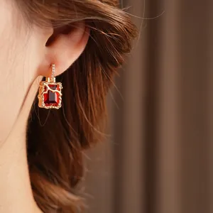 Boucles d'oreilles élégantes en zircon rouge et base dorée texturée sur un mannequin