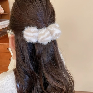 Détail de trois pompons en fausse fourrure crème sur une pince à cheveux d'hiver