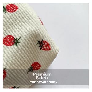 Close-up of high-quality white corduroy fabric with embroidered red strawberry patterns