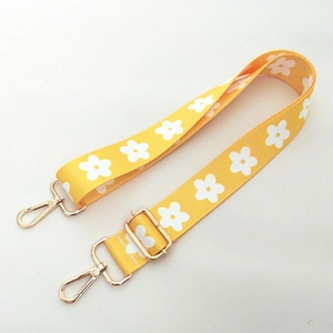 Detail of yellow fabric bag strap with white flower patterns and golden metal buckles