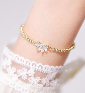 Close-up of a golden beaded bracelet with a butterfly charm made of marquise cut zircons