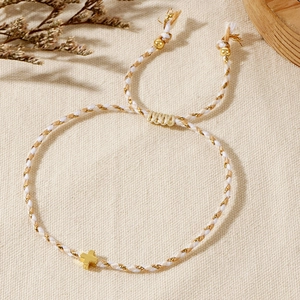 Detail of handmade braided cotton bracelet with gold cross charm on beige canvas background