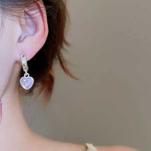 Close-up of heart-shaped earring with purple gemstone and silver latch back closure