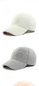 Close-up of fluffy faux fur baseball caps in cream, grey and pink for winter warmth