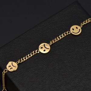Bracelet à breloques souriantes en acier doré sur un coffret cadeau en cuir noir
