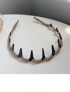 Detail of khaki satin fabric headband with black decorative jagged plastic teeth spikes