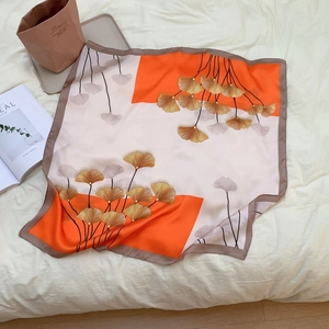 Detail of elegant orange and beige square silk scarf with golden ginkgo leaf pattern