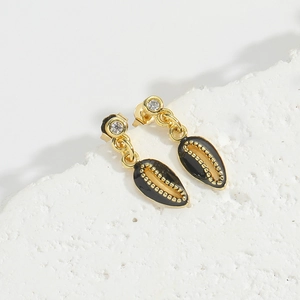 Macro shot of gold shell earrings with black enamel on a textured white rock surface