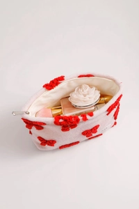 Detail view of white plush cosmetic bag with red bow design and organized inner storage