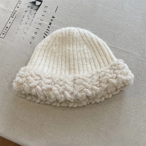 Detail of cream white cable knit winter hat with fluffy faux fur brim on grey linen background