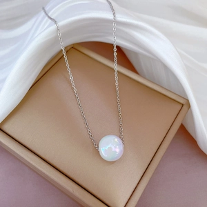Gros plan sur un collier géométrique en acier titane avec perle nacrée blanche sur écrin