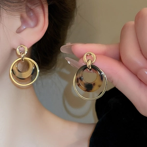 Detail of gold double-hoop earrings featuring tortoiseshell resin drops worn by model