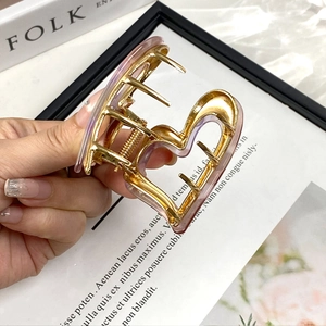 Detailed view of an acetate heart-shaped hair claw clip with golden metal frame and pink finish