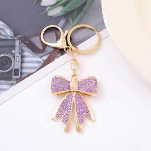 Dettaglio portachiavi a fiocco dorato con strass viola su sfondo bianco pulito