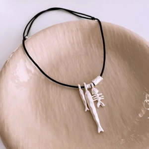 Detail view of fish and fishbone pendants on black cord necklace in a ceramic bowl