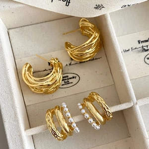 Detail of gold spiral C-shaped earrings and multi-layered faux pearl hoop studs